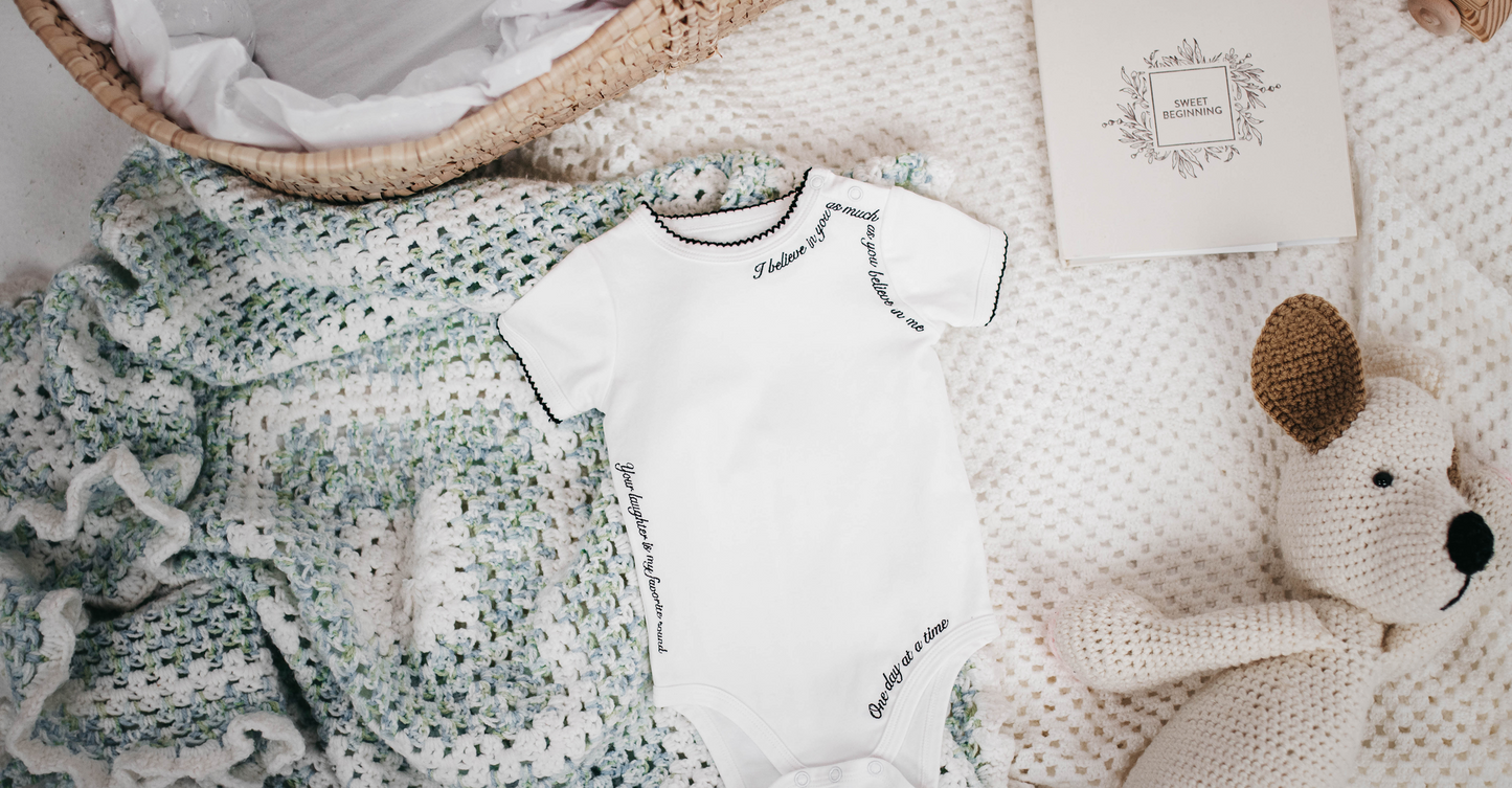 Baby outfit with white onesie, green textured blanket, and stuffed animal on a soft surface.