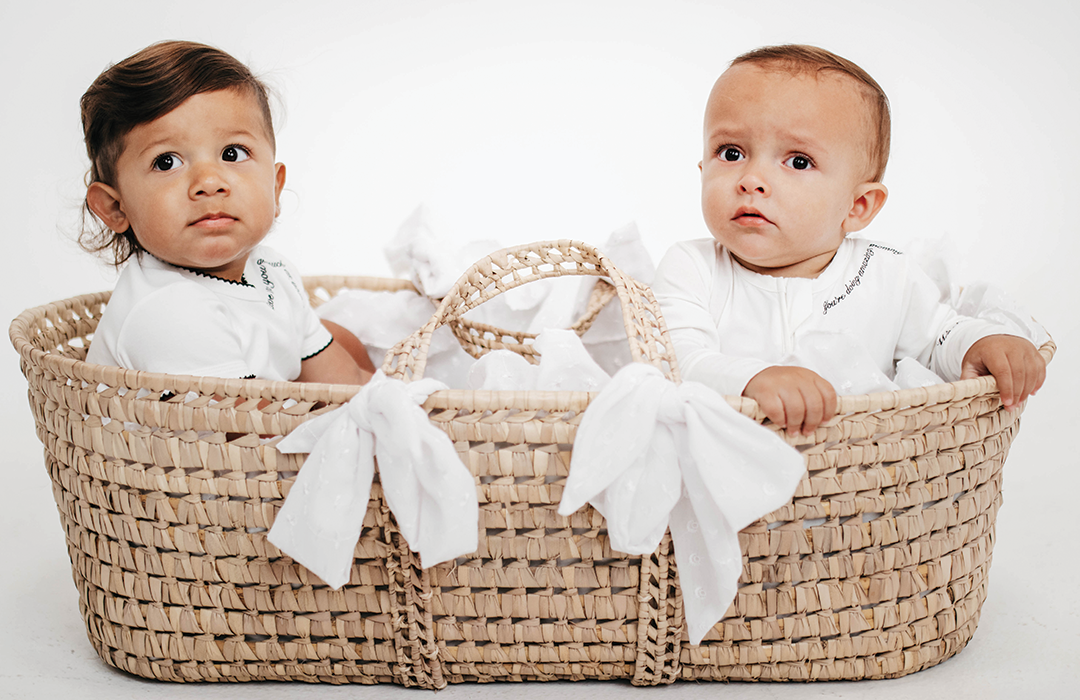 Two babies in a woven basket with white blankets on a plain background